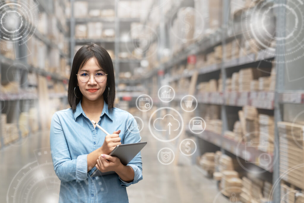 Tangentia|Portrait of happy young attractive asian entrepreneur woman looking at camera using smart tablet in warehouse with inventory management or industry digital era concept. Asian small business or sme.